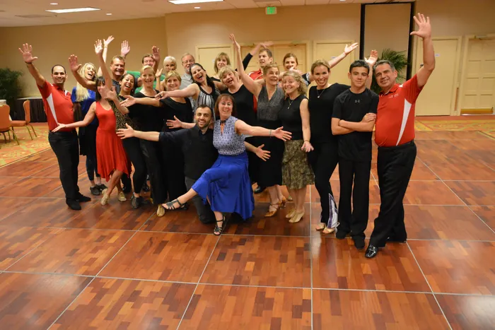 The full dance camp group posed together, most with an arm raised, one woman kneeling in a blue skirt at the front