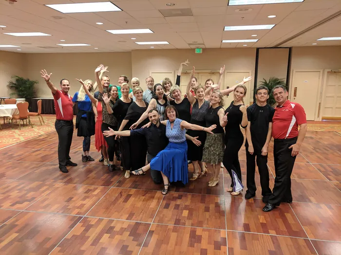The dance camp group gathered for a photo with arms in the air on the ballroom floor