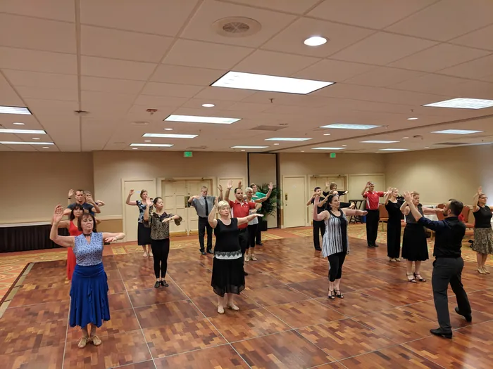 The class spread across the floor with arms raised overhead, following the instructor