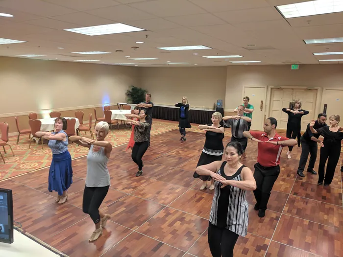 The class in rows practising with arms crossed, seen from the side of the room