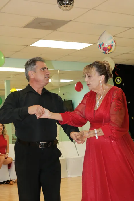 Eleanor in a red gown and Ivan joined at arm's length beneath a mirror ball