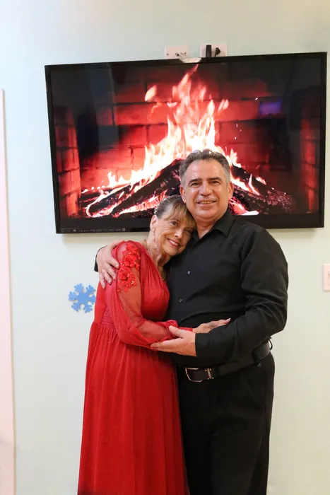 Eleanor in a red dress embracing Ivan in front of the fireplace screen
