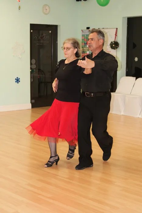 Lourdes in a red skirt and Ivan travelling side by side across the wooden floor