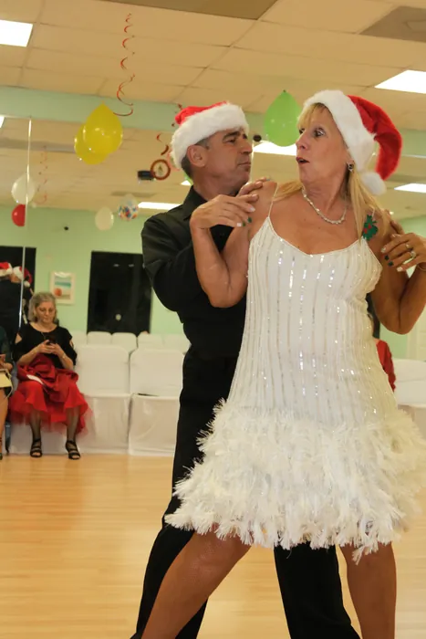Peggie in a white feather dress and Ivan in Santa hats among the hanging decorations
