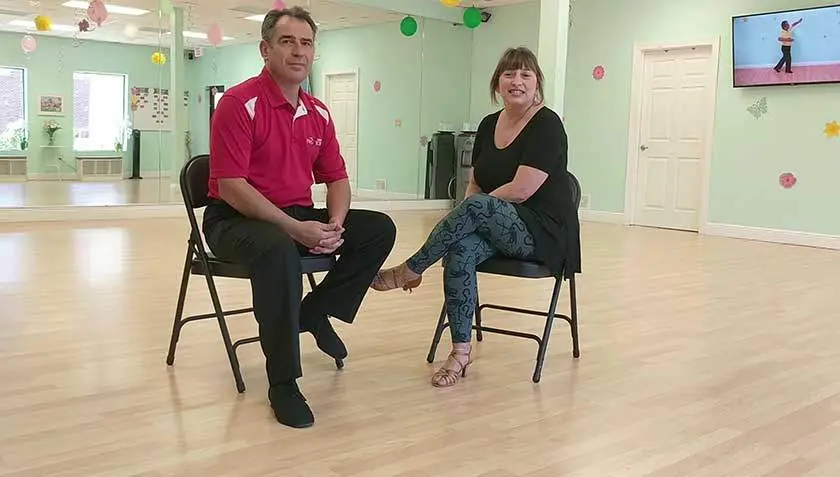 Ivan sitting and talking with a student on the studio floor at Dance Passion