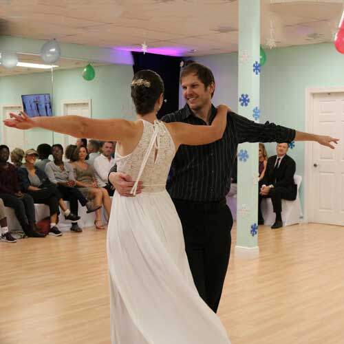 Hilary, in a white dress, dancing with Bryan in front of guests at the Dance Passion studio